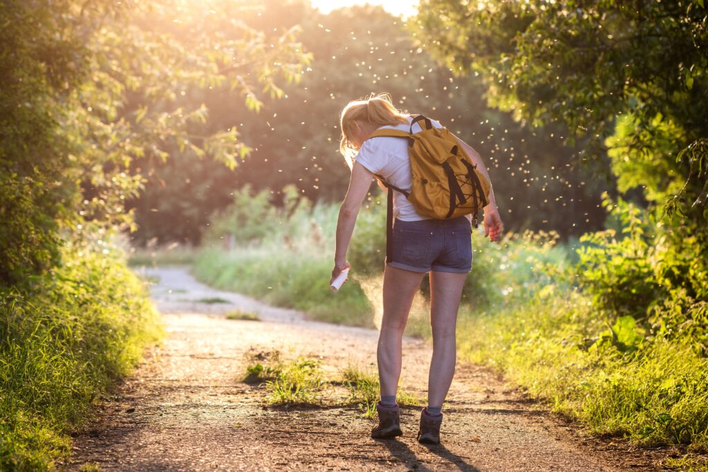 Girl walking in the woods spraying insect repellent to protect against mosquitoes and West Nile virus