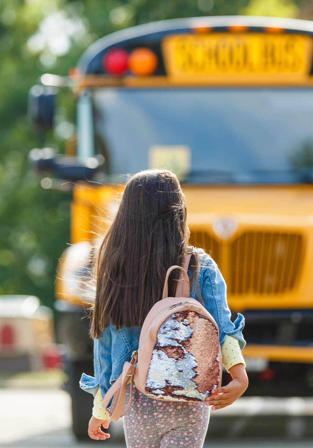 Little girl standing by a big school bus door with her pink backpack.