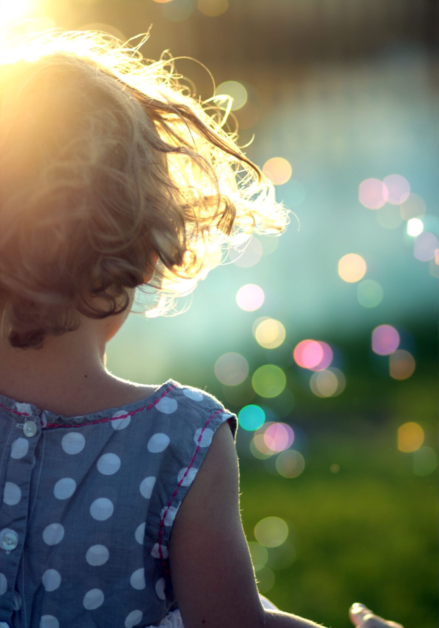 Back of a young child facing a sunburst and bubbles floating in the air